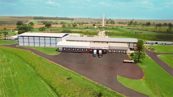 Uma fotografia aérea da Friovale. Temos três caminhões de logística fria estacionados no pátio. Ao fundo, temos as instalações da empresa.